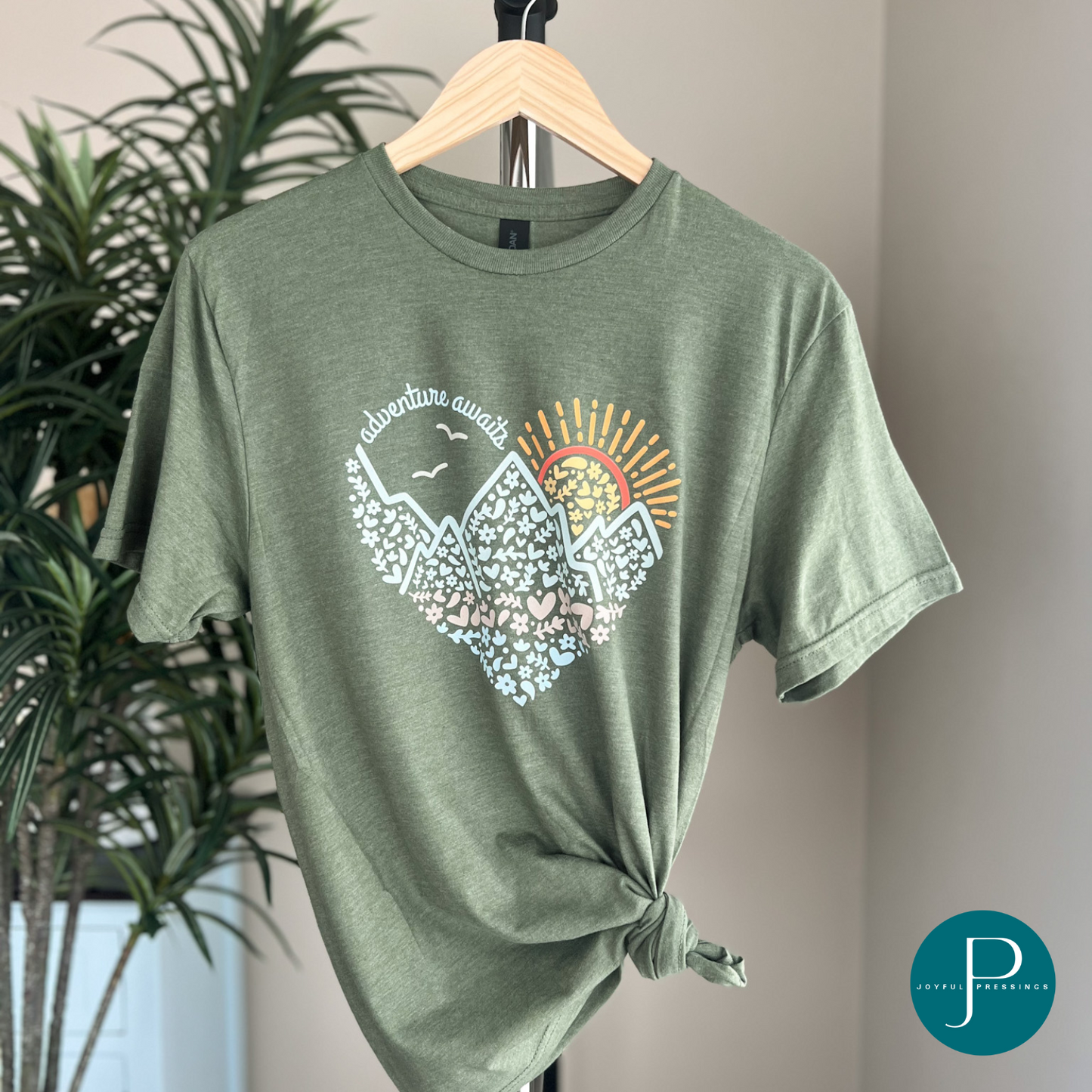 hanging display of adventure awaits print on a gildan softstyle cactus green tee.