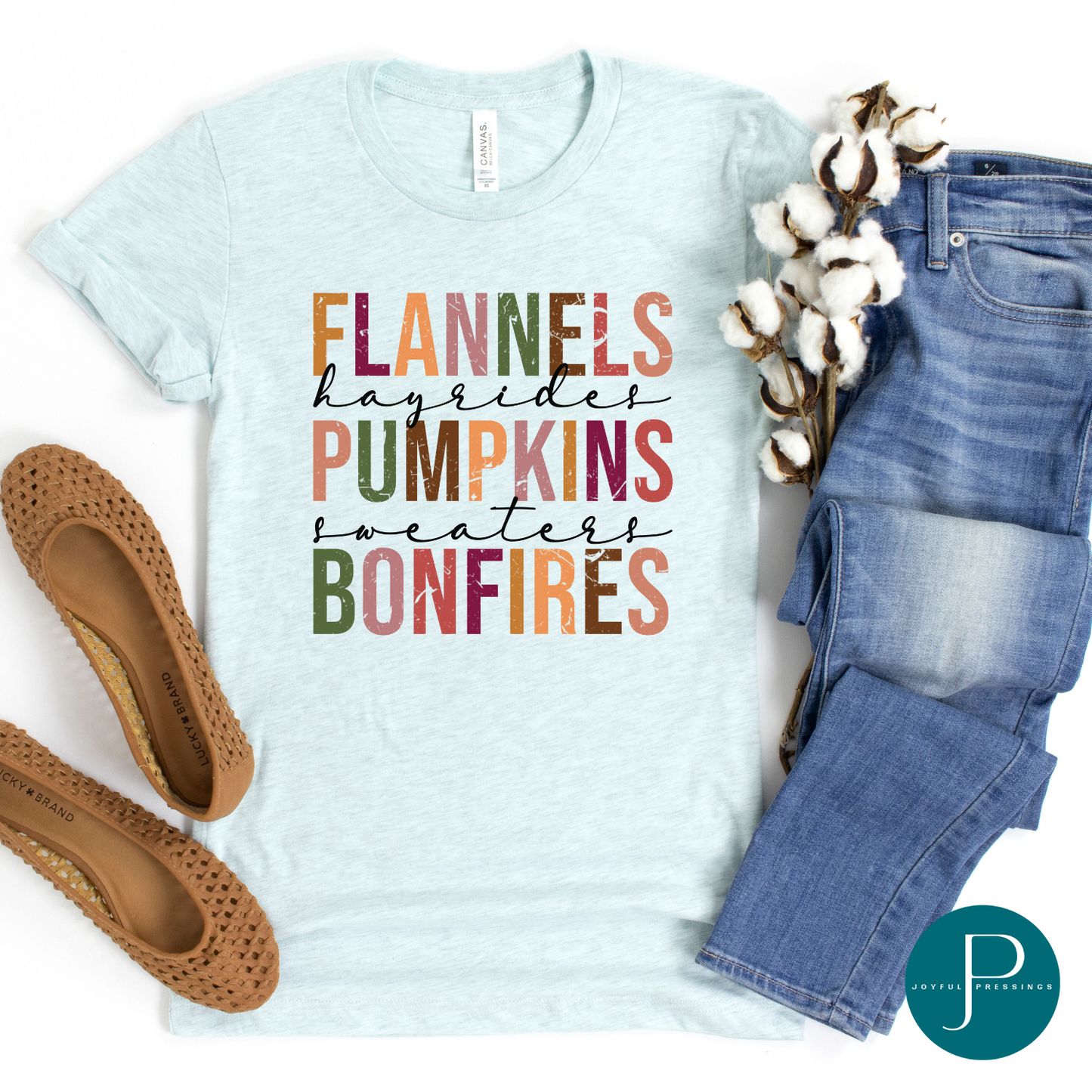 Flat-lay of Ice Blue t-shirt with the print flannels, hayrides, pumpkins, sweaters, and bonfires.